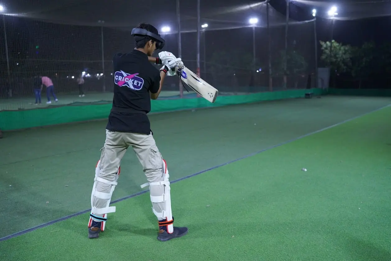 A batter in CricketX kit training at night with a real bat and a Quest headset